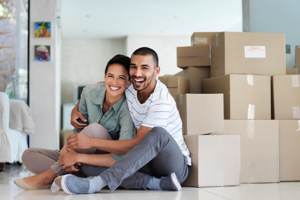 Couple smiling in new home with boxes surrounding them 